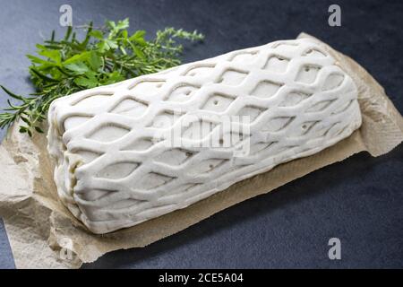 Bistecca di maiale cruda Kasseler come pezzo in pasta sfoglia con erbe come closeup offerto su carta marrone e sfondo nero con spin. copia Foto Stock