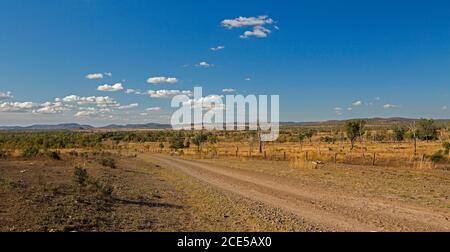 Vista panoramica dell'arido paesaggio australiano dell'entroterra durante la siccità strada di ghiaia rossa che si estende attraverso pianure a distanze lontane sotto cielo blu Foto Stock