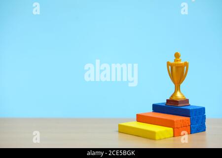 Trofeo d'oro in piedi sul colorato podio su un tavolo di legno Foto Stock