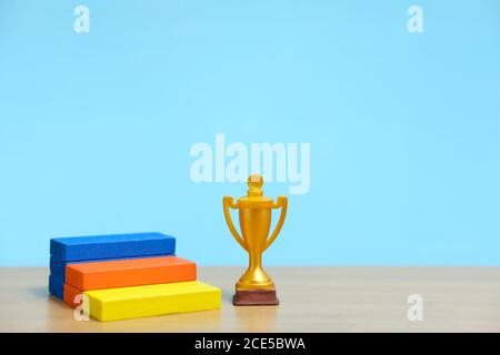 Trofeo d'oro in piedi accanto al colorato podio su un tavolo di legno Foto Stock