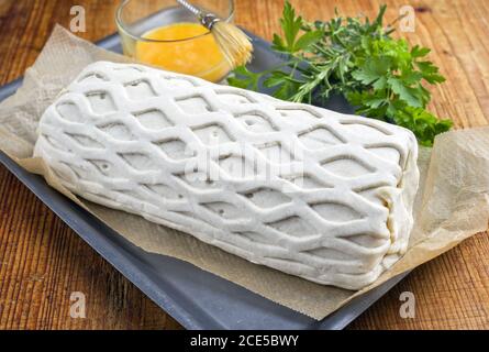 Carne di maiale cruda Kasseler come pezzo in pasta sfoglia e. tuorli d'uovo come closeup offerto su una griglia con le erbe Foto Stock