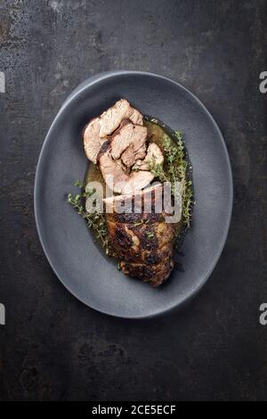 Arrosto di agnello greco marinato al barbecue con erbe in salsa al sugo come vista dall'alto su una piastra di design moderna con copia spazio Foto Stock