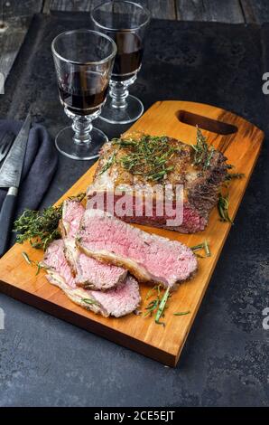 Arrosto domenicale tradizionale del Commonwealth con fette di manzo arrosto a fette fredde con erbe e vino rosso come primo piano su un moderno taglio del progetto Foto Stock