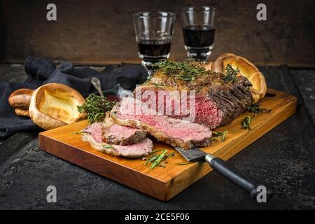 Arrosto domenicale tradizionale del Commonwealth con fette di manzo arrosto a fette fredde Con erbe e Yorkshire pudding closeup su un desi moderno Foto Stock