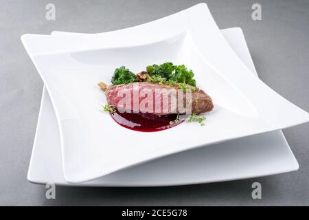 Fritto secco invecchiato filetto di cervo filetto medaglione bistecca naturale con kalette e salsa di lamponi come closeup su un design moderno Foto Stock