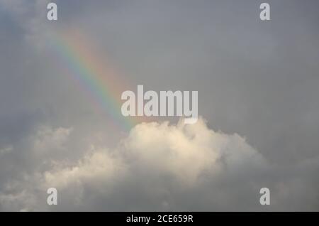 Un breve arcobaleno alto nelle nuvole scure del luce serale mentre il sole è in fase di tramontare Foto Stock