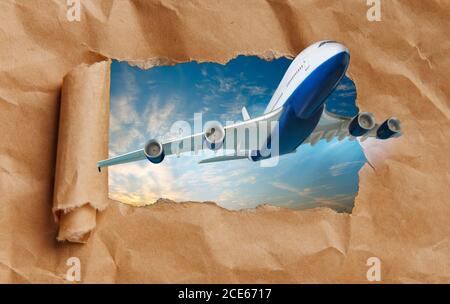 Aereo che vola attraverso la carta strappata. Concetto di trasporto aereo e di viaggio. Foto Stock