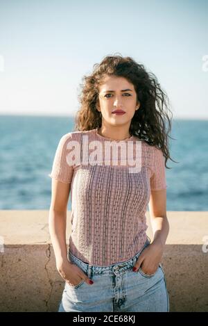 Donna giovane seria in piedi vicino alla spiaggia che si loking alla macchina fotografica Foto Stock