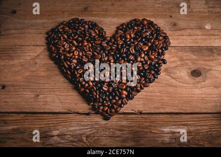 Vista dall'alto di chicchi di caffè aromatici disposti su un tavolo di legno a forma di cuore Foto Stock