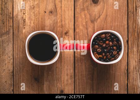 Vista dall'alto composizione di tazze rosse con caffè aromatico torrefatto fagioli e fresco caldo energizzante americano messi insieme su legno tabella Foto Stock