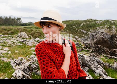 Donna viaggiatore in rosso poncho lavorato a maglia e cappello a piedi  Collina erbosa mentre godendo le vacanze nelle Asturie in Spagna Foto stock  - Alamy