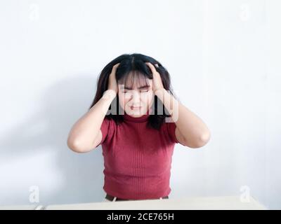 Ritratto di una giovane donna stressata che tiene la testa in mano con lo sfondo. Infelice ragazza asiatica con preoccupato stressato espressione del volto guardando verso il basso. Foto Stock