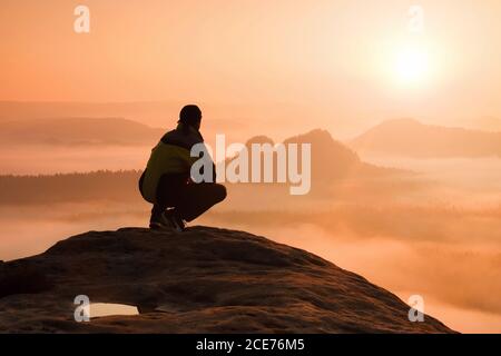 Vista posteriore dell'escursionista maschile seduto sulla cima rocciosa mentre vi godete una colorata pausa da giorno sopra la valle dei tumrains Foto Stock