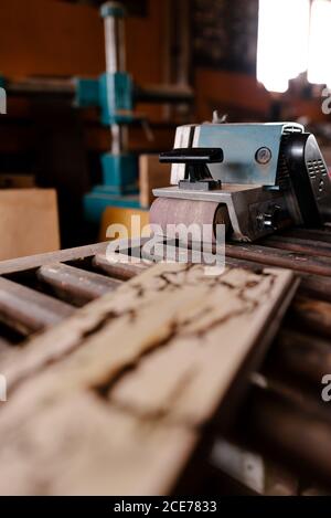 Levigatrice a nastro professionale posizionata su un tavolo di legno vicino al legno affondo in officina di scabvicino Foto Stock