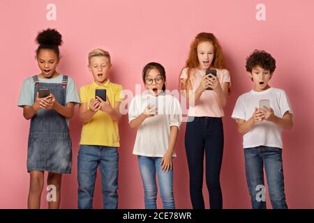 Scioccato scolari che guardano nei loro telefoni cellulari su sfondo rosa Foto Stock