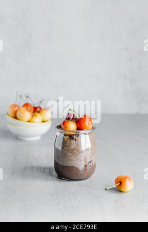 Vasetto di vetro con budino di cioccolato composto da yogurt e chia semi e guarniti con ciliegia bianca Foto Stock