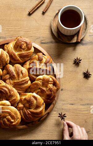 Vista dall'alto del raccolto femmina su tavola di legno con mucchio di focaccine dolci e bastoncini di cannella disposti con una tazza di caffè e anice stellato Foto Stock