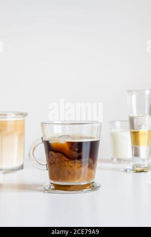 Caffè fresco aromatico ghiacciato con latte servito in tazza di vetro su tavolo decorato con fiori Foto Stock