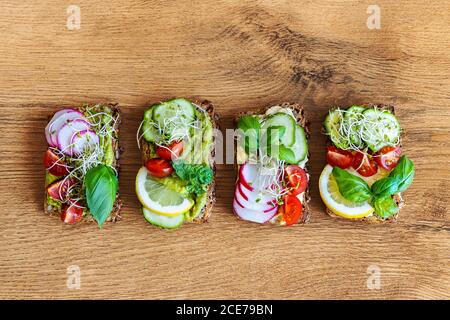 Vista dall'alto di deliziosi toast con fette di ravanello e limone guarnito con ciuffi di basilico e posto su tavola di legno dentro cucina Foto Stock