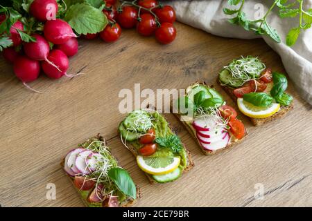 Vista dall'alto di deliziosi toast con fette di ravanello e limone guarnito con ciuffi di basilico e posto su tavola di legno dentro cucina Foto Stock