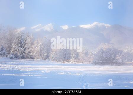 Foresta invernale, recinzione in legno, picchi di montagna Foto Stock