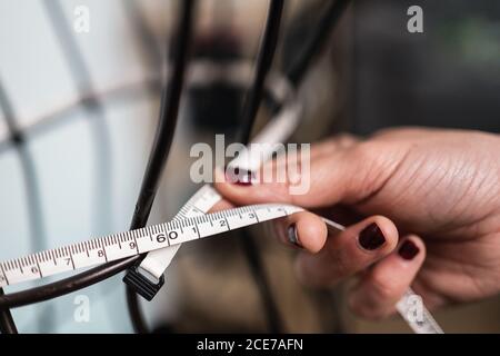 Seamstress tagliato e non riconoscibile che misura il finto filo in piedi monolocale in stile loft Foto Stock