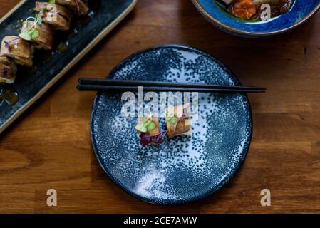 Dall'alto di involtini appetitosi con riso e salmone guarnito con erbe fresche e posto su piatto con chopsticks di bambù nel ristorante Foto Stock