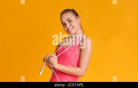 Ragazza atletica felice in posa con Jump Rope su sfondo giallo Foto Stock