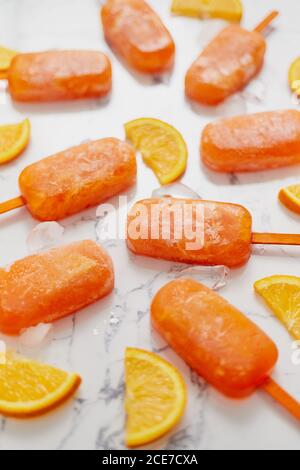 Pop sicle surgelate fatte in casa con arance fresche oragniche poste con cubetti di ghiaccio sul tavolo di marmo Foto Stock