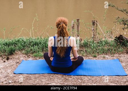 Giovane donna che fa yoga vicino al fiume da solo. Sport in blocco. Vista posteriore. Foto Stock