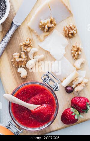 Da sopra vista closeup della tavola con marmellata di fragole in un vaso, formaggio a fette e formaggi assortiti serviti su tavola di legno Foto Stock