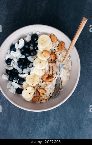 Vista dall'alto della ciotola di porridge con mandorle crude, banana a fette, mirtilli e cocco grattugiato Foto Stock