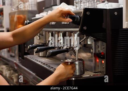 Vista laterale di una barista femminile non riconoscibile che utilizza la macchina da caffè e. preparazione di caffè aromatico in caffetteria Foto Stock