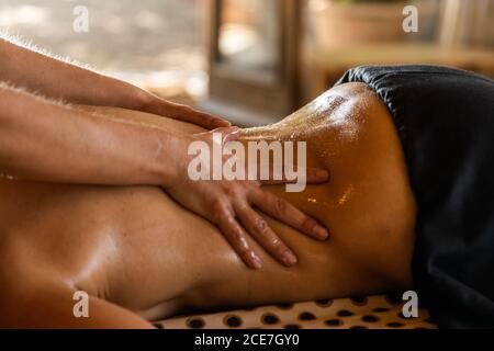 Vista laterale del raccolto anonimo master che esegue massaggio ayurvedico con olio aromatico sul retro di clienti rilassati in un salone moderno Foto Stock