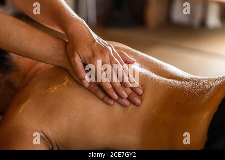 Vista laterale del raccolto anonimo master che esegue massaggio ayurvedico con olio aromatico sul retro di clienti rilassati in un salone moderno Foto Stock