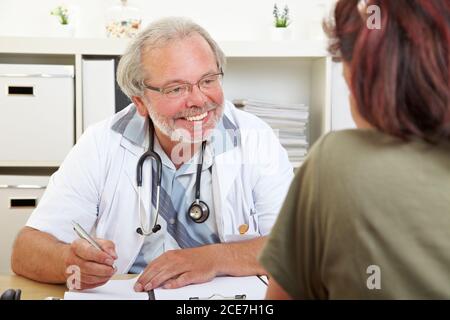 Un medico amichevole alla scrivania nella sua pratica consiglia un pazienti anziani Foto Stock