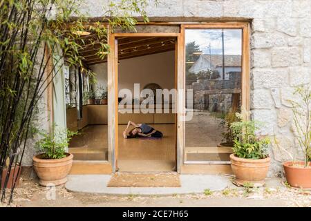 Femmina in abbigliamento sportivo seduto in rotazione angolo seduto mentre si pratica Shakti yoga da solo in studio luminoso con interni in legno resort tropicale Foto Stock