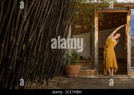 Donna serena in piedi nella porta nel cortile e facendo il lato piegatevi mentre praticate lo yoga Foto Stock