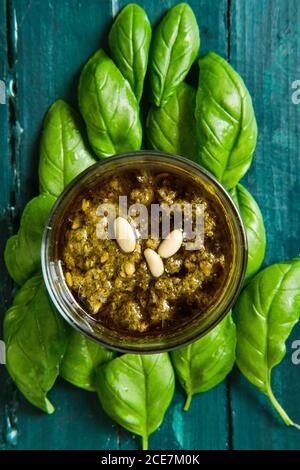 Vista dall'alto di una piccola ciotola di vetro con il famoso pesto italiano salsa fatta di foglie di basilico fresco e pinoli ricoperti con olio d'oliva Foto Stock