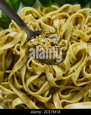 Da sopra cucchiaio con salsa al pesto e gustosa pasta italiana su piastra in ceramica decorata con foglie di basilico fresco su legno tabella Foto Stock