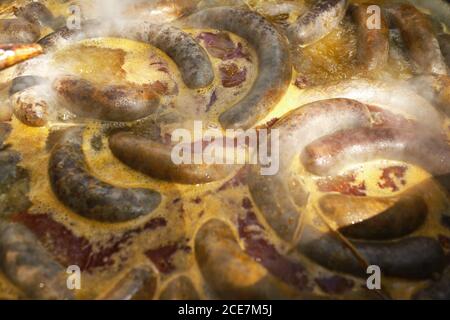 Processo di cottura delle salsicce di sangue in pentola di ferro su falò nella tradizionale fabbrica di carne in zona rurale Foto Stock