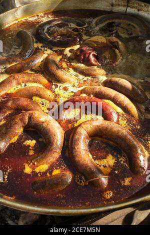 Processo di cottura delle salsicce di sangue in pentola di ferro su falò nella tradizionale fabbrica di carne in zona rurale Foto Stock