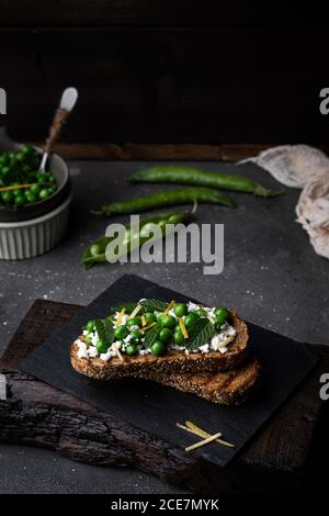 Ancora vita di piselli e toast di formaggio servito su un piastra di ardesia su sfondo scuro Foto Stock