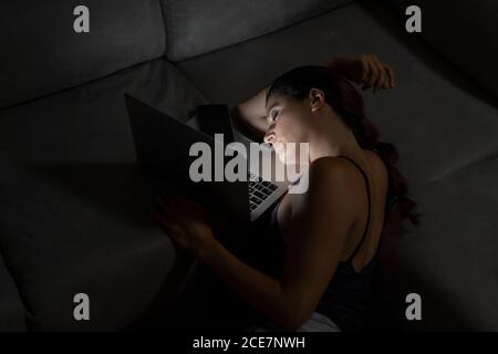 Sfinito freelancer femminile appoggiandosi sul divano con laptop e coppa di bevanda calda mentre si lavora da casa a distanza Foto Stock