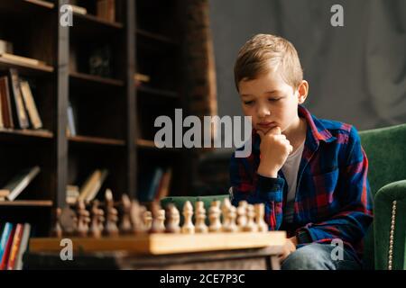 Ritratto in primo piano di un ragazzino intelligente penoso che pensa al prossimo spostarsi sulla scacchiera Foto Stock