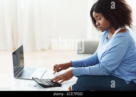 Donna nera che usa la calcolatrice e il pc a casa Foto Stock