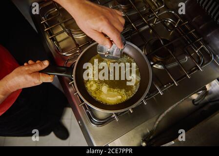 Da sopra di raccolto anonimo chef che versa olio d'oliva da il metallo può entrare nella padella con il burro fuso durante la preparazione cibo in cucina Foto Stock