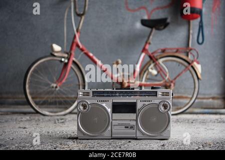 Riproduttore portatile di nastri a cassetta singola vecchio stile posizionato su cemento pavimento contro la bicicletta sfocata rossa e la parete grigia dello shabby dentro garage Foto Stock