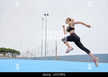 Vista laterale a basso angolo di una giovane atleta sicura in outfit fitness che salta su un terreno sportivo Foto Stock