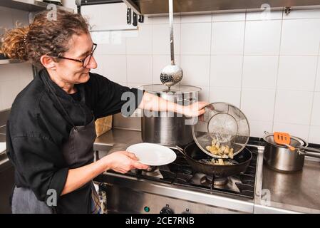 Donna cuoca in bicchieri frittura carciofi nella cucina di un ristorante. Foto Stock